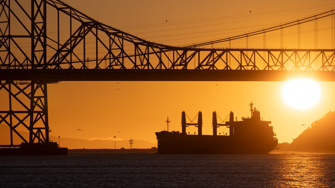 A large crude oil tanker moves slowly across a calm sea under an overcast sky.