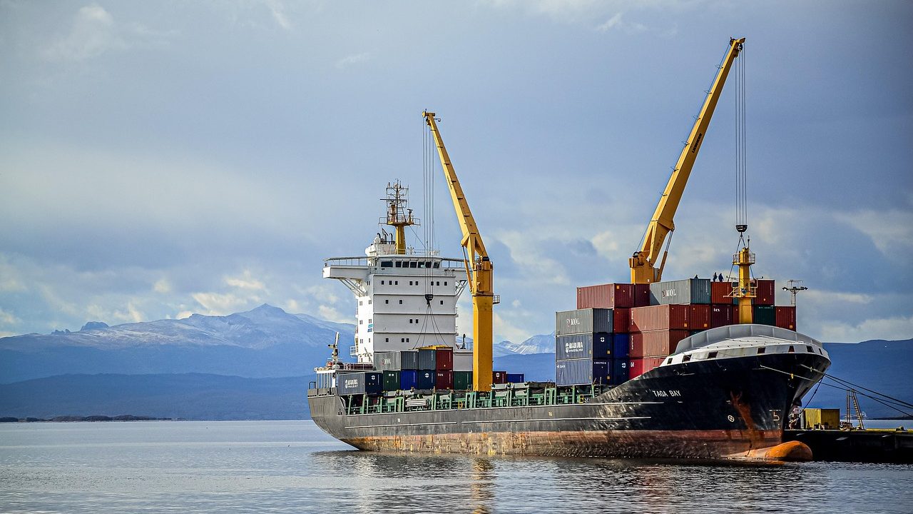 A large cargo vessel moves across dark open water beneath a cloudy sky.