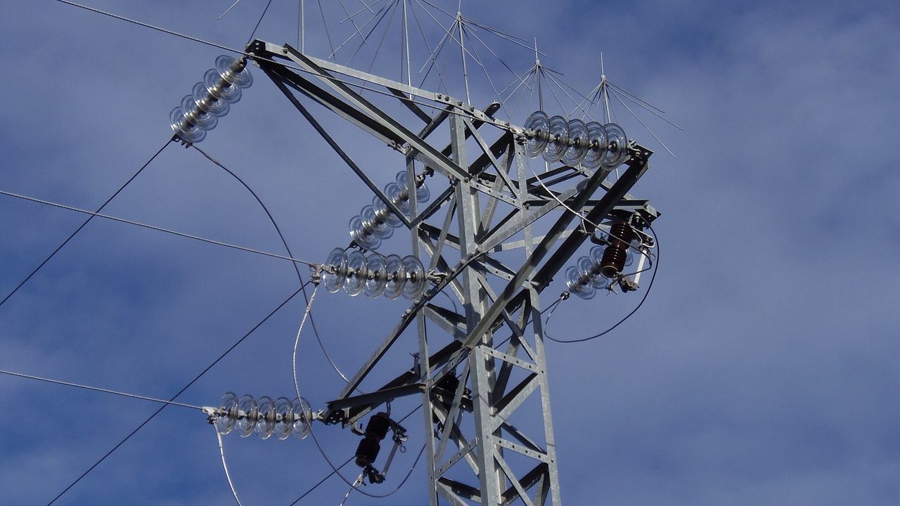 High-voltage electrical substation with transmission towers against a gray sky.