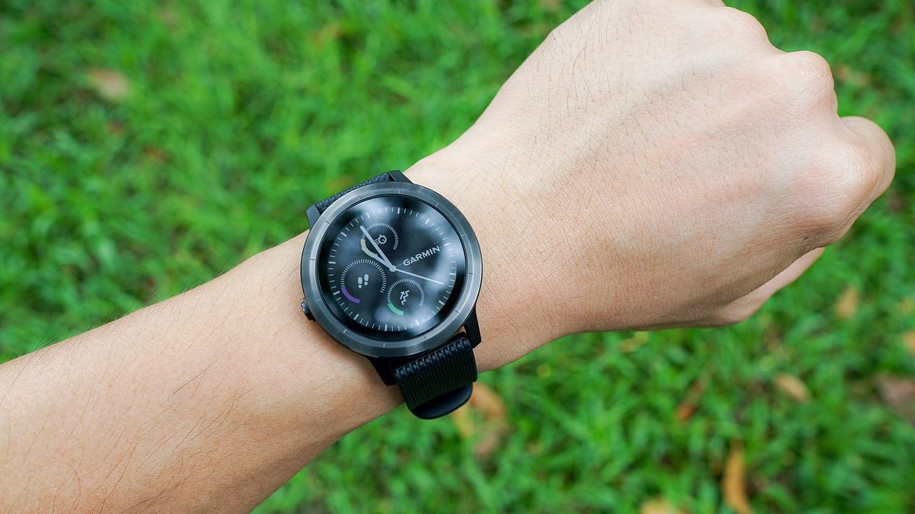 A sleek smartwatch with a glowing display sits on a person's wrist against a neutral background.