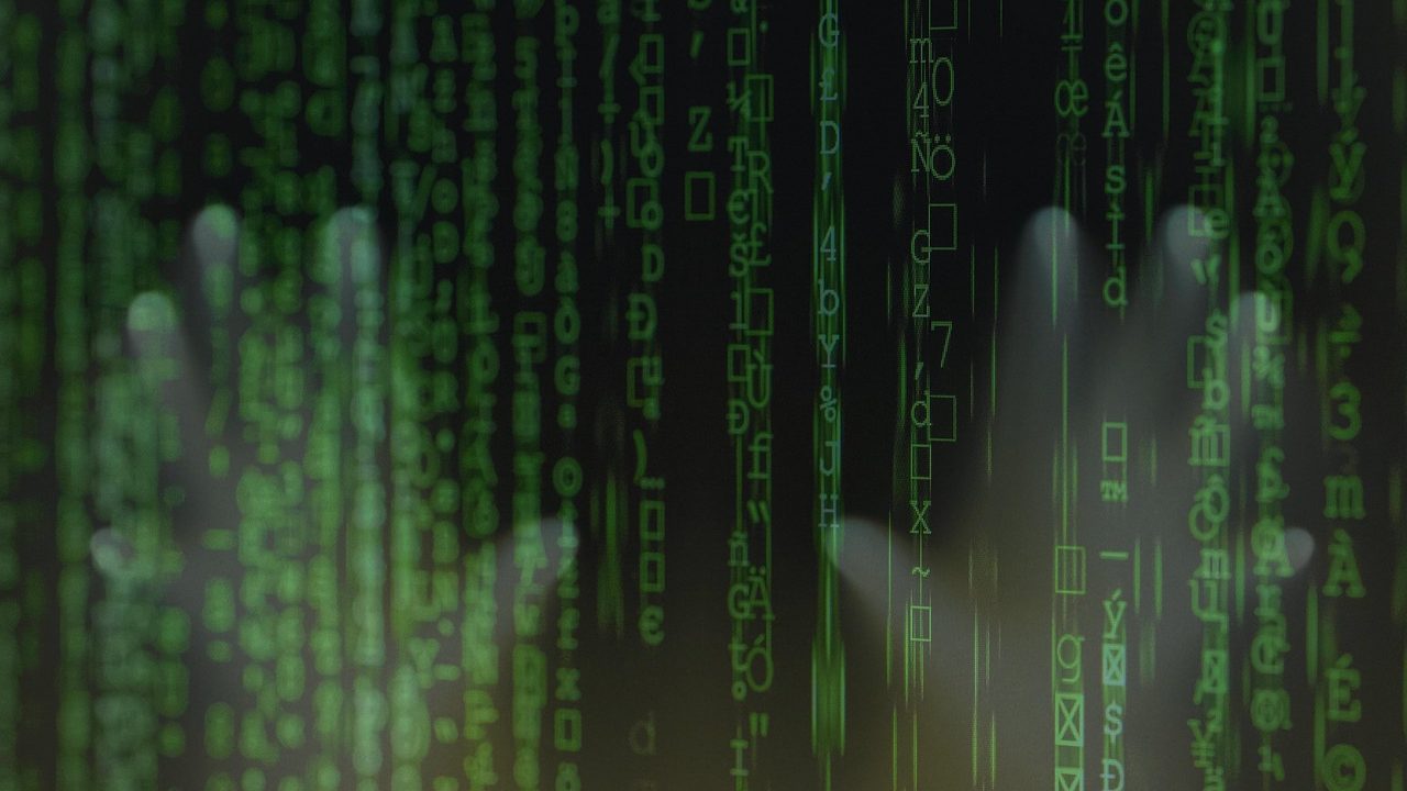 Glowing lines of code scroll across a dark computer monitor in a dim room.