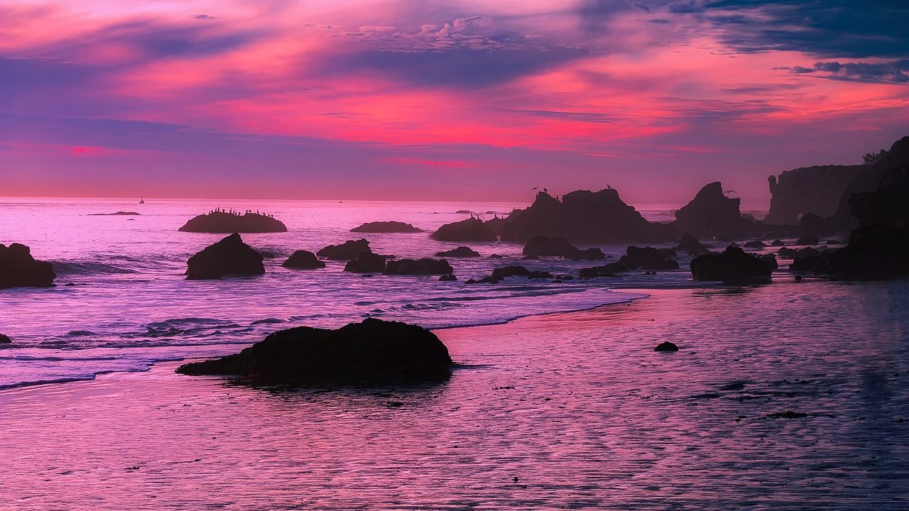 Large waves crashing against a rocky Southern California coastline under stormy skies.
