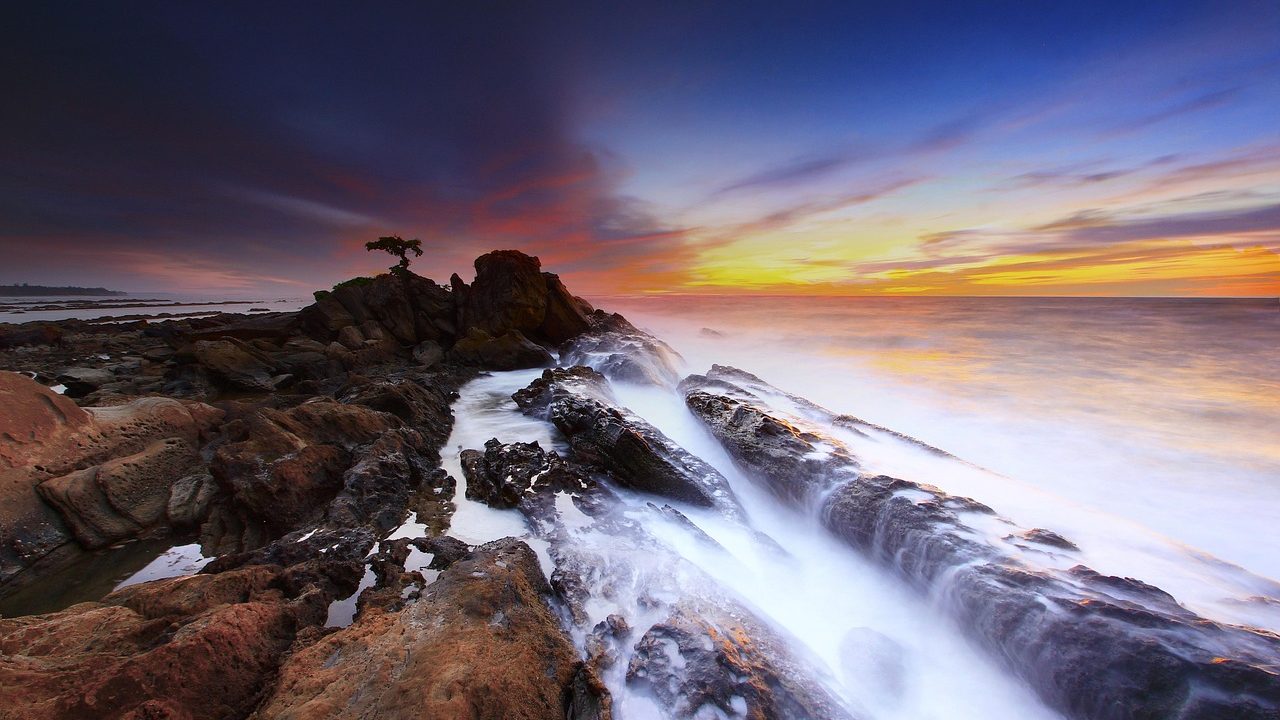 Massive ocean waves crashing against a rocky coastline under a stormy sky.