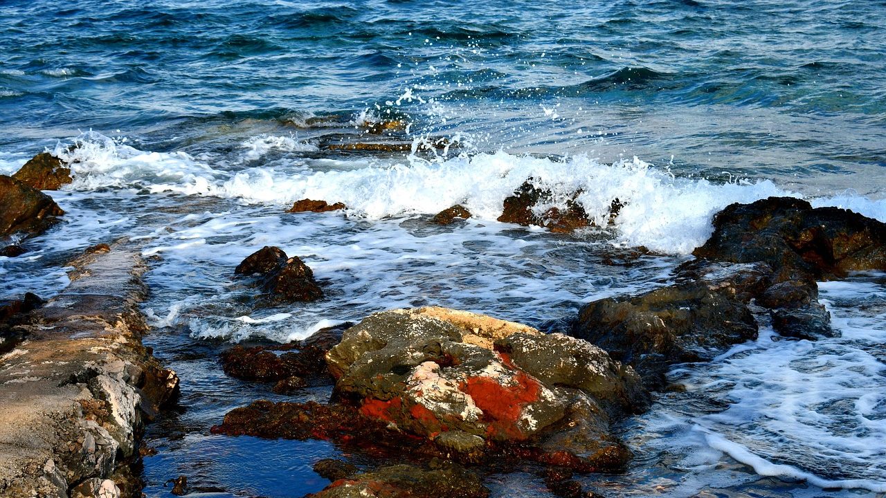 Large waves crash onto a sandy beach under partly cloudy skies.