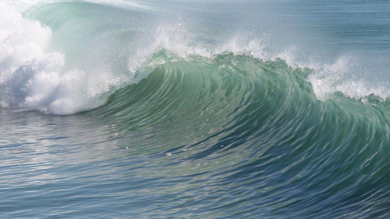 Large waves crash on a Southern California beach under cloudy skies.