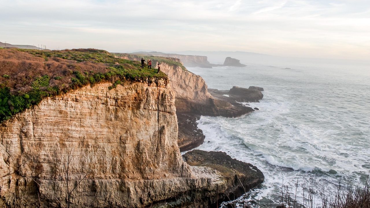A sunny Southern California coastline with calm waves and a clear blue sky over the Pacific Ocean.