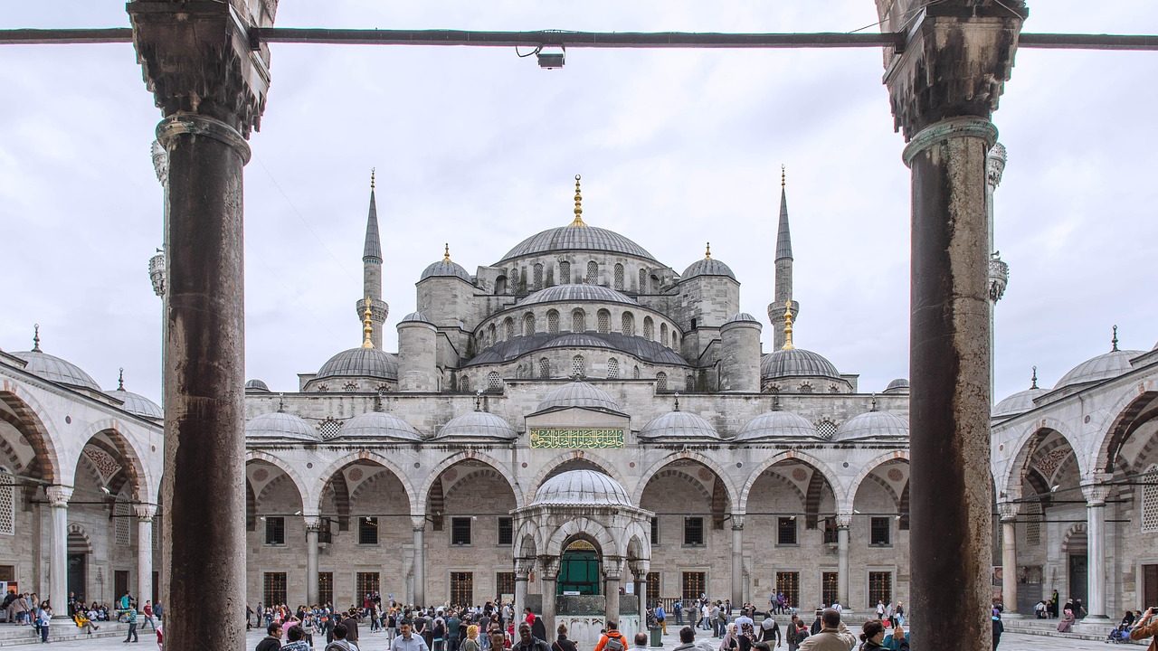 Exterior of a domed mosque building with arched entryway under clear sky.