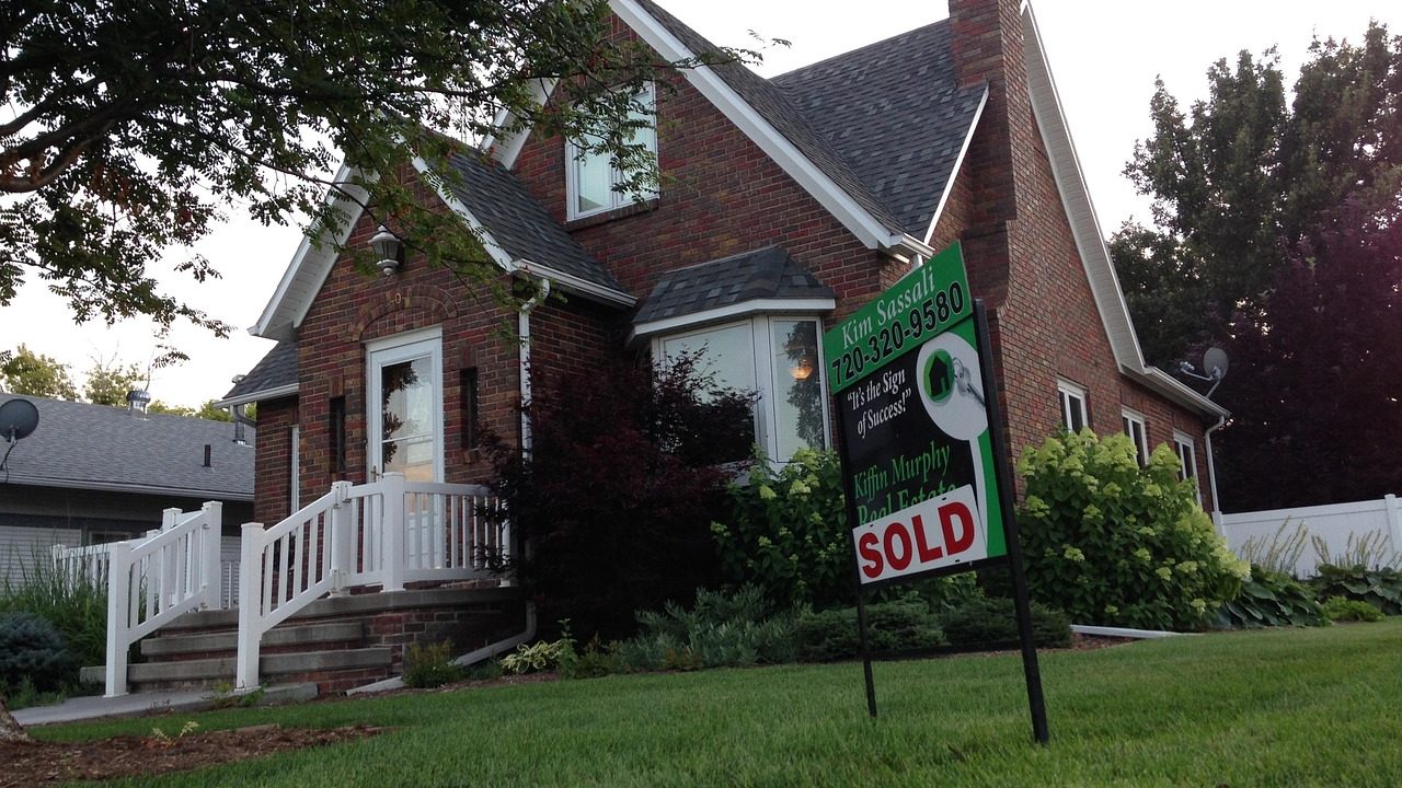 A row of single-family homes with a for-sale sign on a quiet residential street.