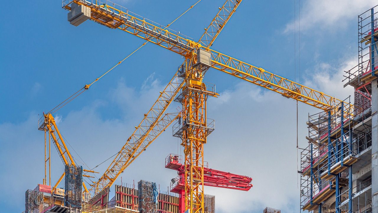 Multiple construction cranes rise above a large residential development site on open land.