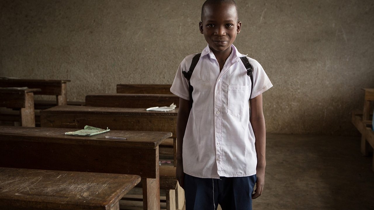A student works on an open laptop at a classroom desk surrounded by notebooks and pencils.