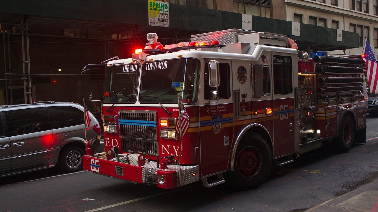 A red fire engine parked on a city street with hoses extended.