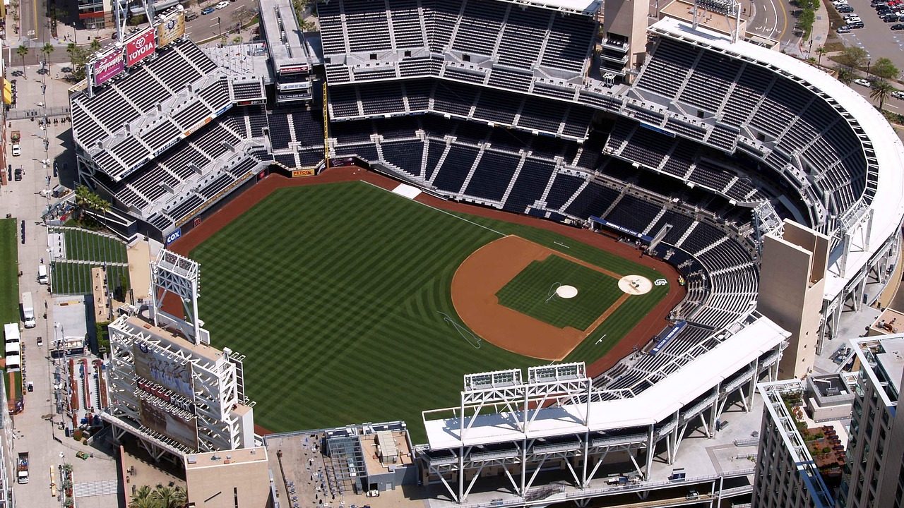An empty baseball stadium with green field and blue seats under clear sky.