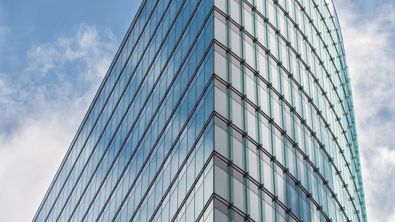 A modern glass corporate office building under a partly cloudy sky.