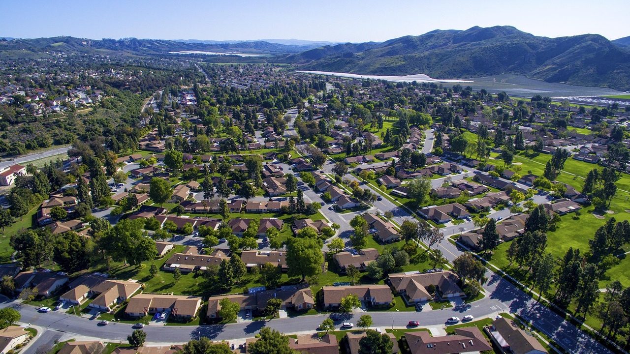 A grassy neighborhood park with trees and benches on a clear day.