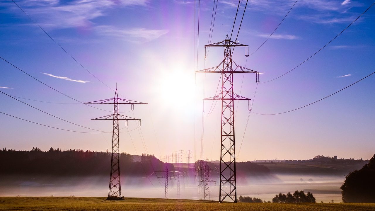 High-voltage transmission towers and power lines stretch across an open landscape at dusk.