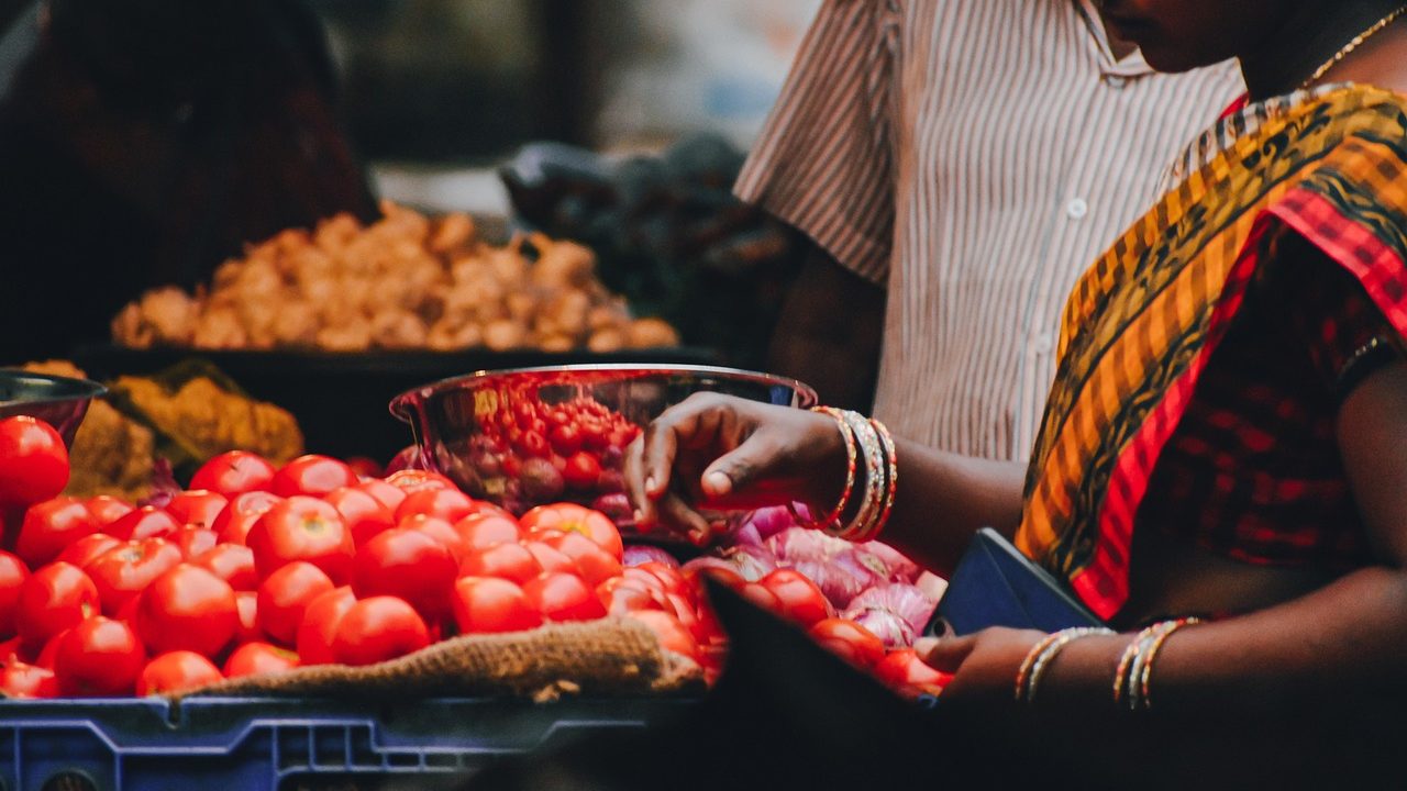 Colorful produce stalls and shoppers fill an outdoor farmers market on a sunny morning.