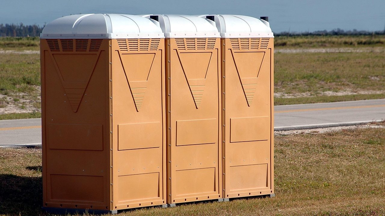 A concrete public restroom building stands at the edge of a sunny urban park.