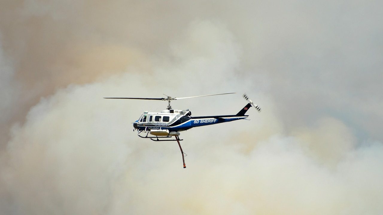A firefighting aircraft drops a plume of red retardant over a hillside fire.