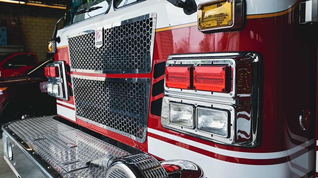 A fire engine parked inside a bright fire station bay with overhead doors open.