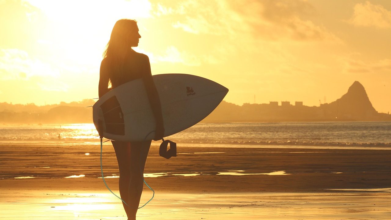 A surfer riding a wave during a competitive surfing event with judges' tents visible on the beach.
