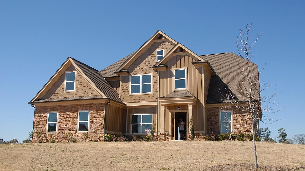 A residential house with a real estate for-sale sign posted on the front lawn on a sunny day.