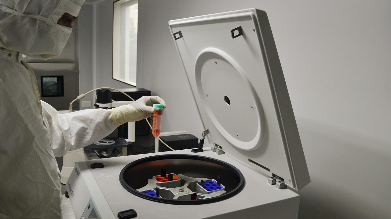 Scientists work at lab benches surrounded by research equipment and glassware in a modern biotech facility.