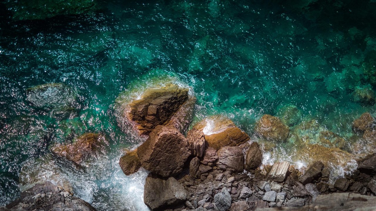 Rugged coastal cliffs with white ocean surf breaking against dark rock at the base.
